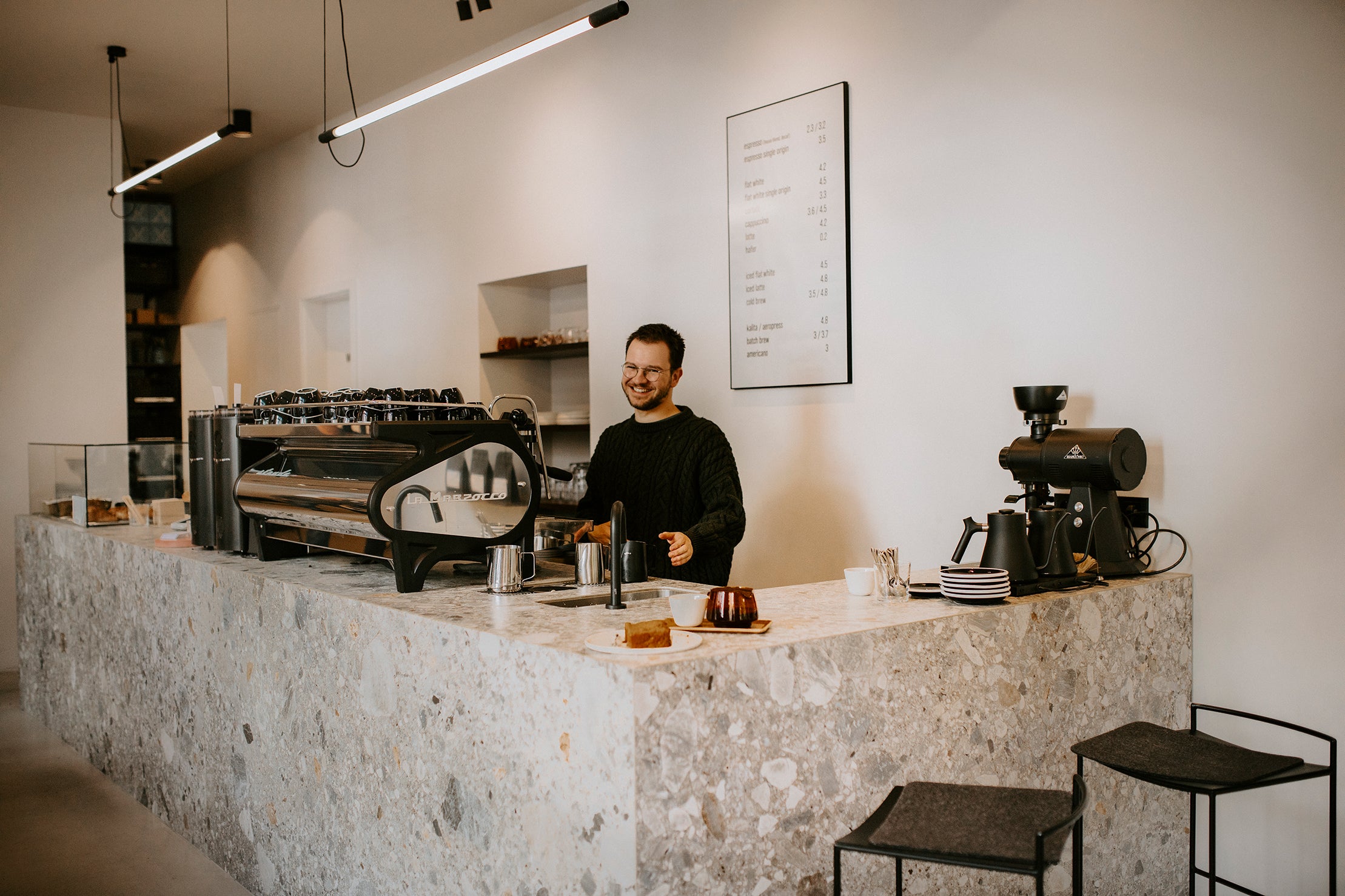 Lächelnder Barista hinter der Theke in der Ernst Kaffeeröster Kaffeebar in Köln Sülz